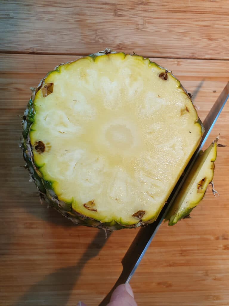 starting to slice the skin off the pineapple with the top already cut off.