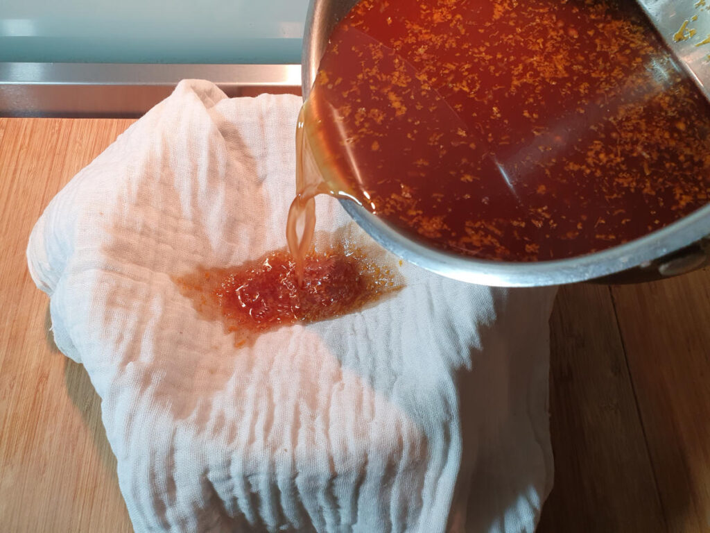 straining cola through a cheesecloth lined sieve over a bowl.