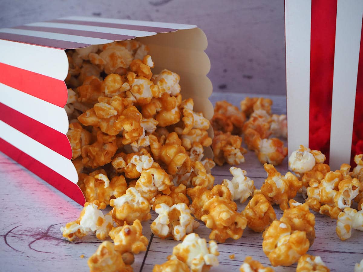 Red and white striped box of caramel popcorn tipped over with caramel popcorn scattered out and another red and white stripped box next to it.