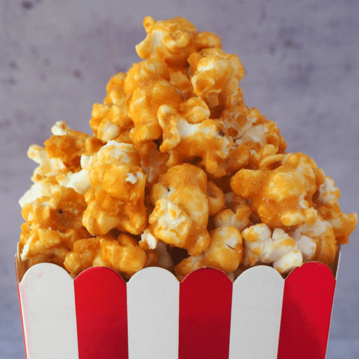 Close of up caramel popcorn pilled in a red and white striped box.