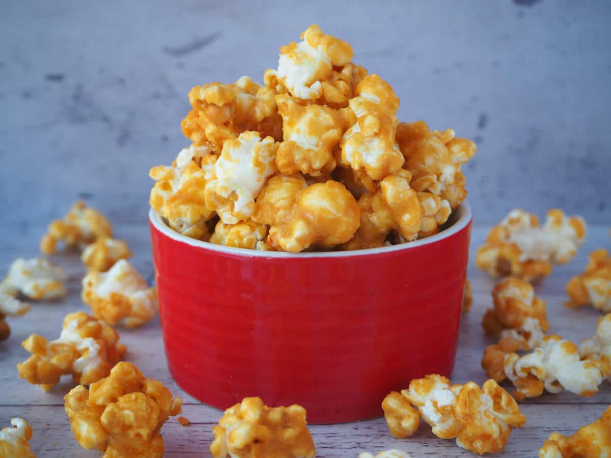 Caramel popcorn in a red bowl with caramel popcorn scattered around it.