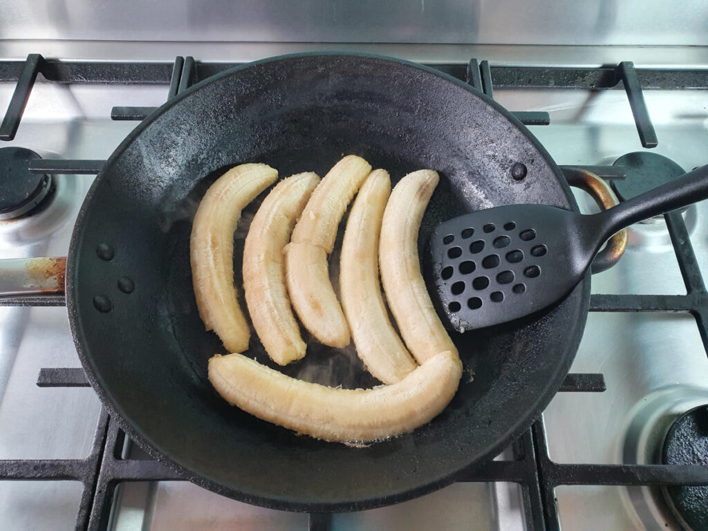 Flipping cooked bananas in frying pan with spatula.