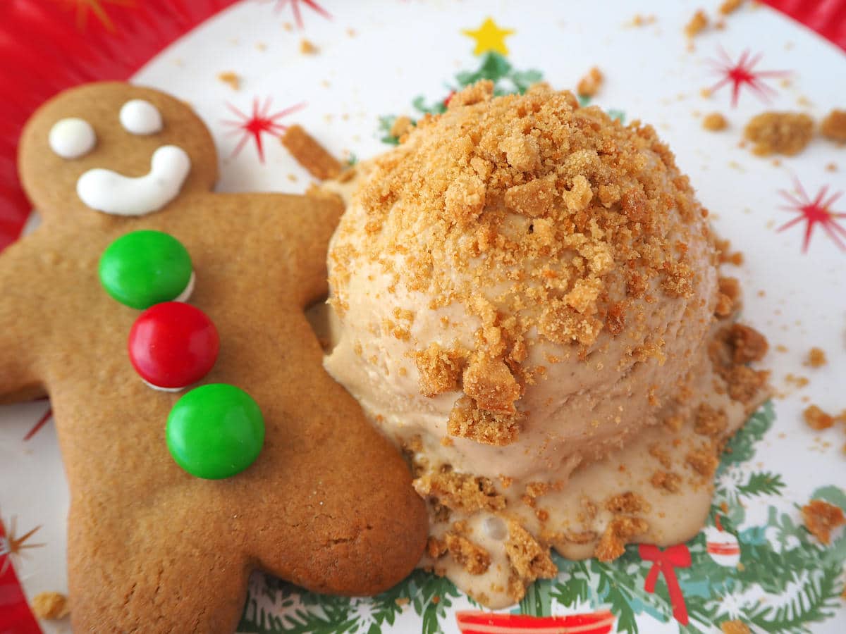 Scoop of gingerbread ice cream with crushed gingerbread on top, on a Christmas place, with a gingerbread man next to it.