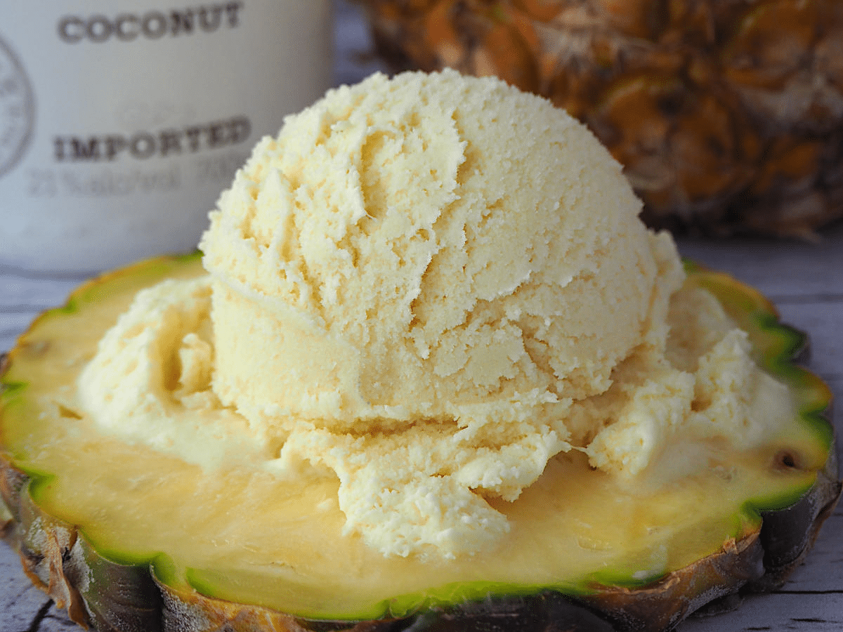 scoop of pina colada ice cream on pineapple slice, with coconut rum and pineapple in background.