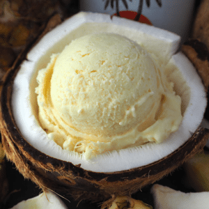 Scoop of pina cola ice cream in half a coconut, with pineapple and coconut rum bottle in background.
