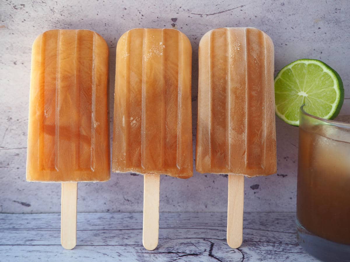 Cola popsicles 2 Row of three cola popsicles standing up next to a glass of homemade cola with a round lime garnish.