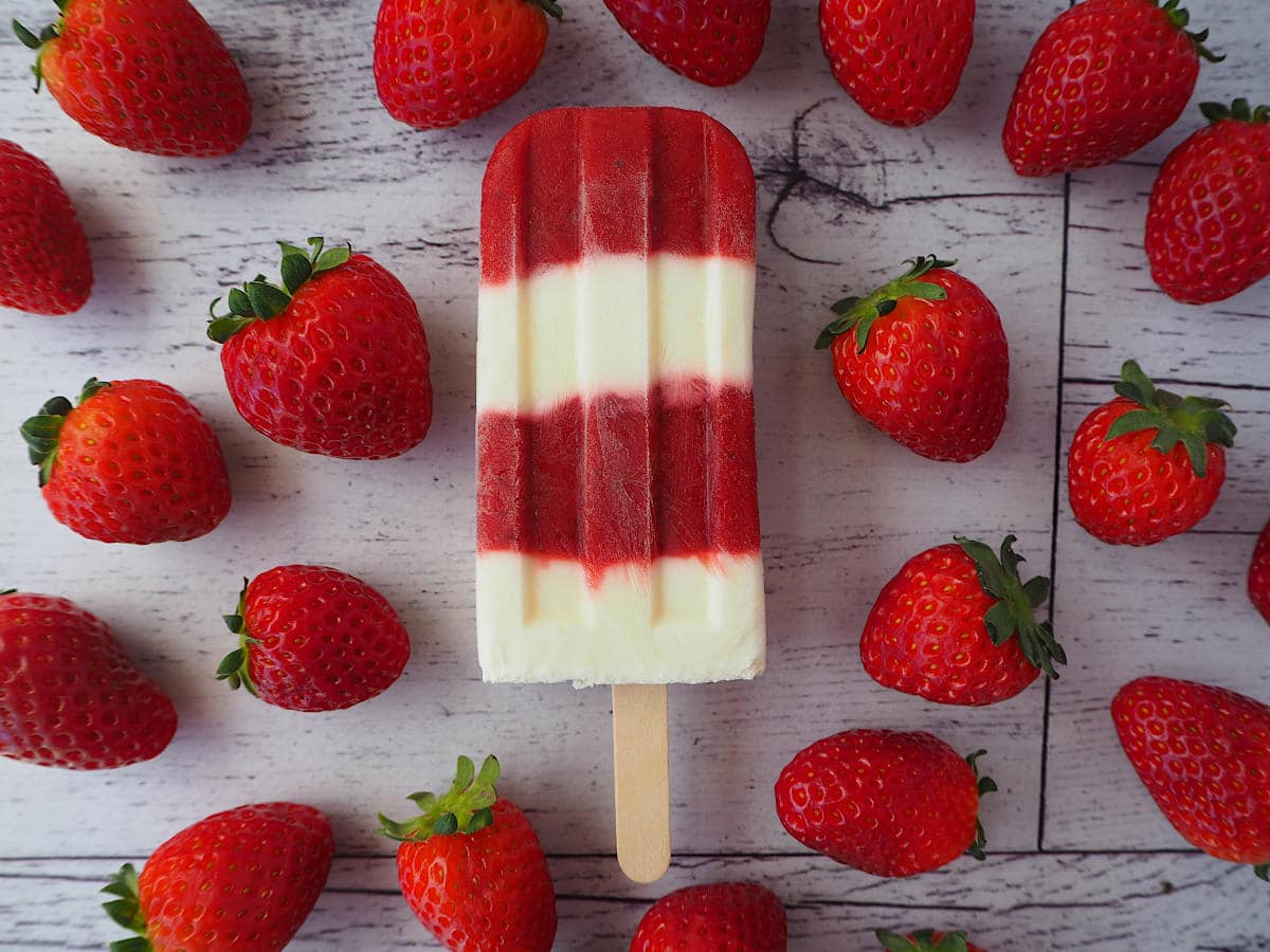 Single strawberry yogurt popsicle surrounded by strawberries.