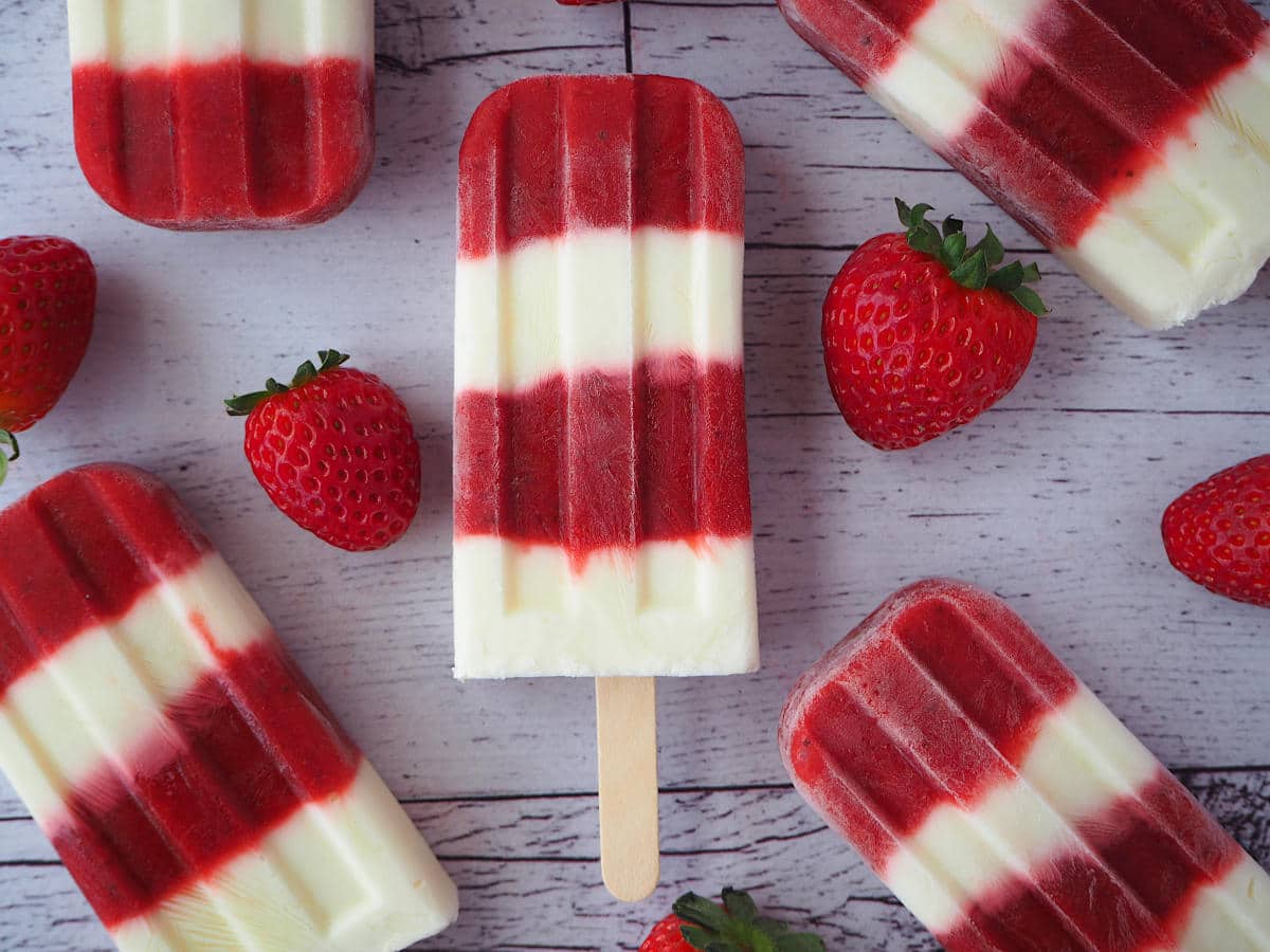 Strawberry yogurt popsicles in haphazard pattern surrounded by strawberries.