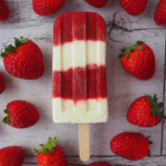 Single strawberry yogurt popsicle surrounded by strawberries.