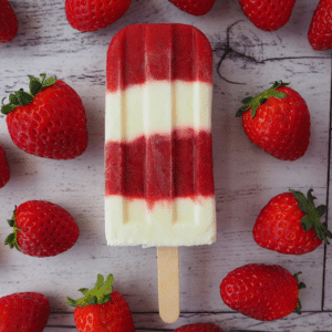 Single strawberry yogurt popsicle surrounded by strawberries.