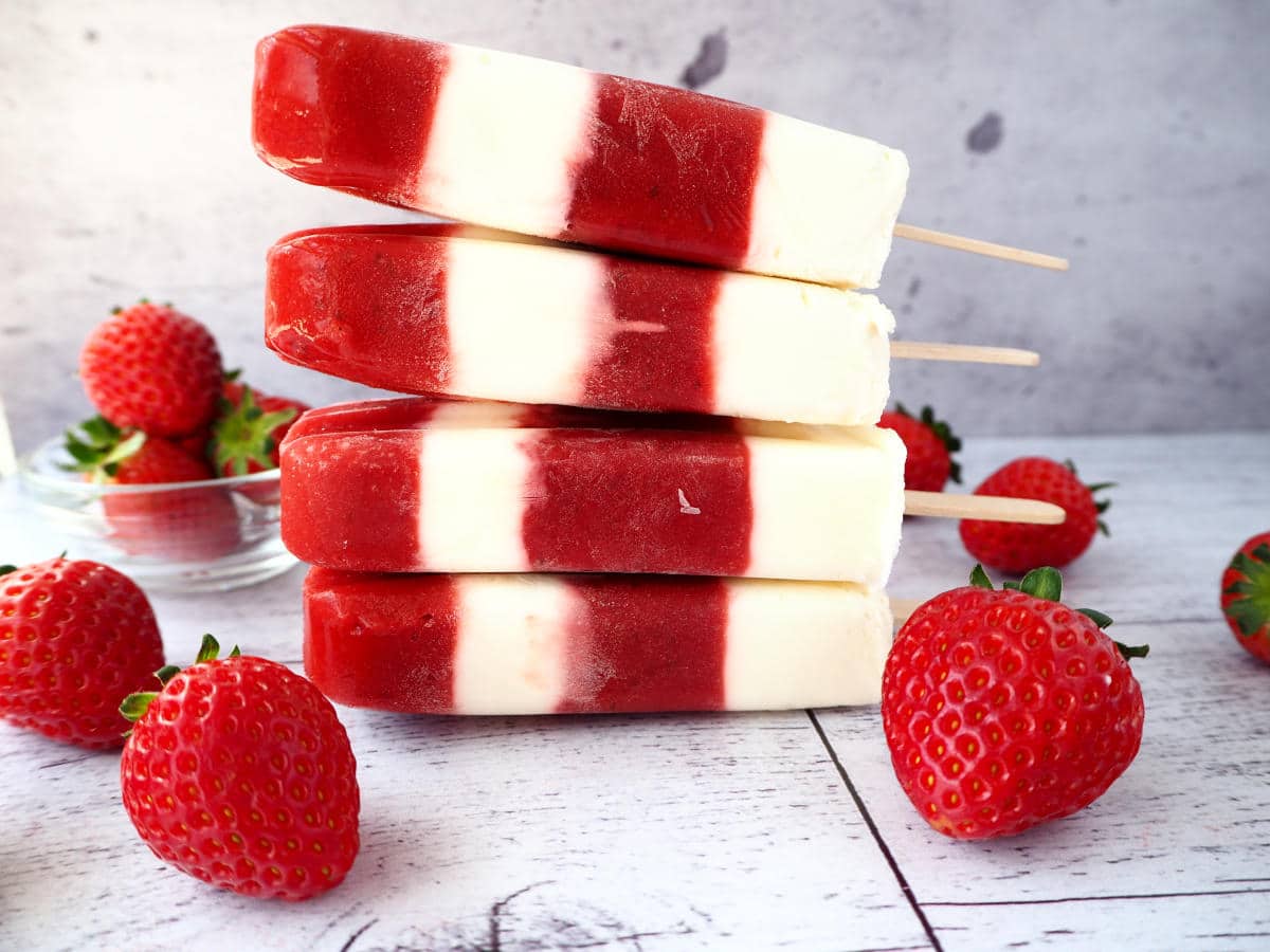 Stack of four strawberry yogurt popsicles surrounded by strawberries.