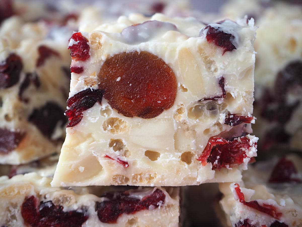 Close of view of side of white Christmas showing pretty ingredients inside, large red cherries, white almonds, cranberries and rice bubbles, set in white chocolate.
