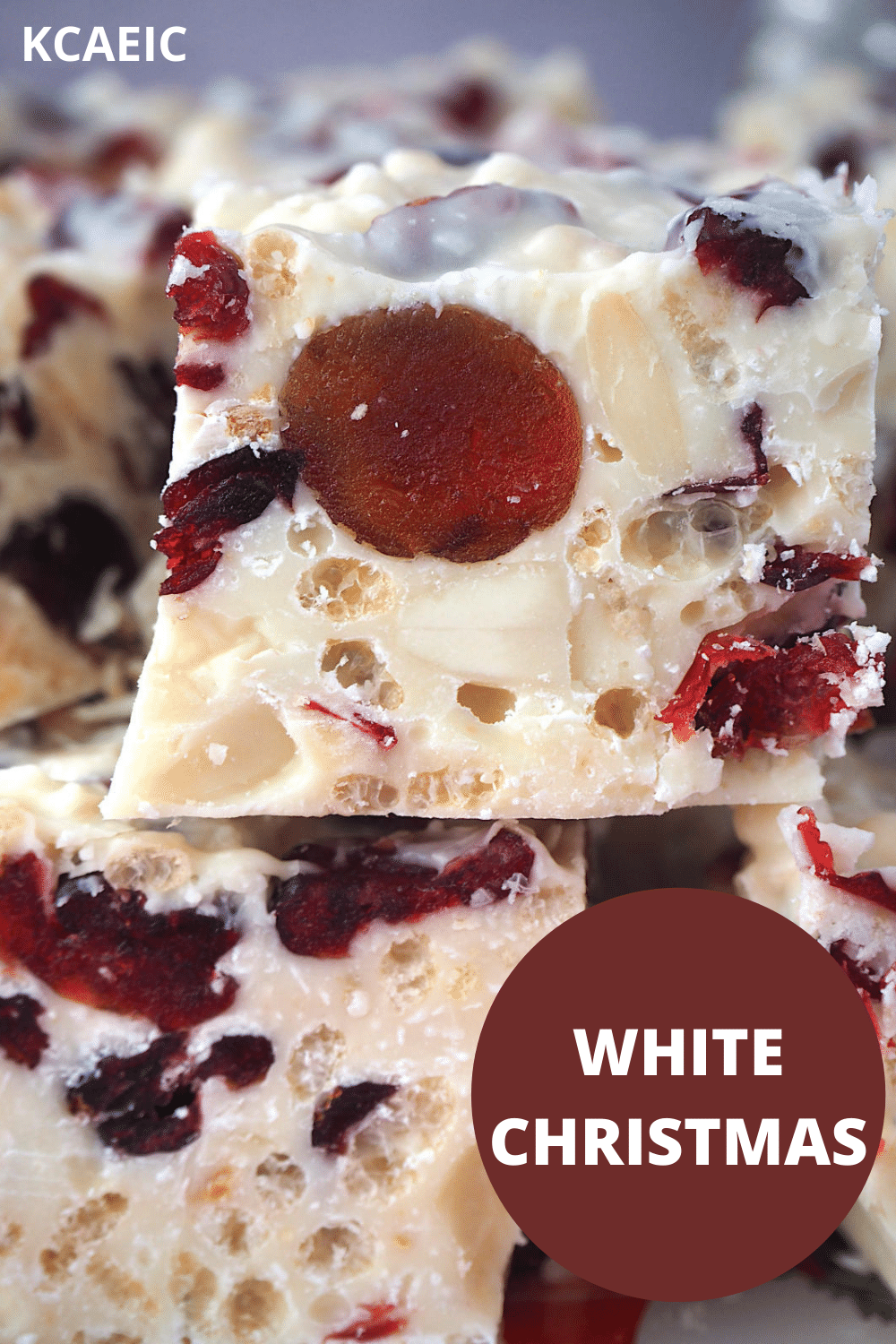 Close of view of side of white Christmas showing pretty ingredients inside, large red cherries, white almonds, cranberries and rice bubbles, set in white chocolate, with text overlay, White Christmas and KCAEIC.