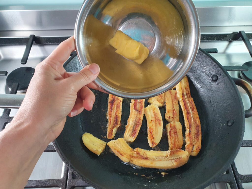 Adding butter to bananas in frying pan on stove.