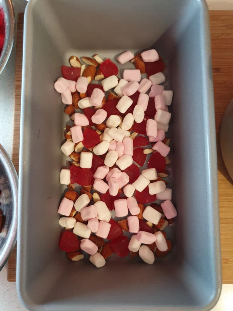 adding first layer of mini marshmallows to bottom of chilled ice cream storage container.