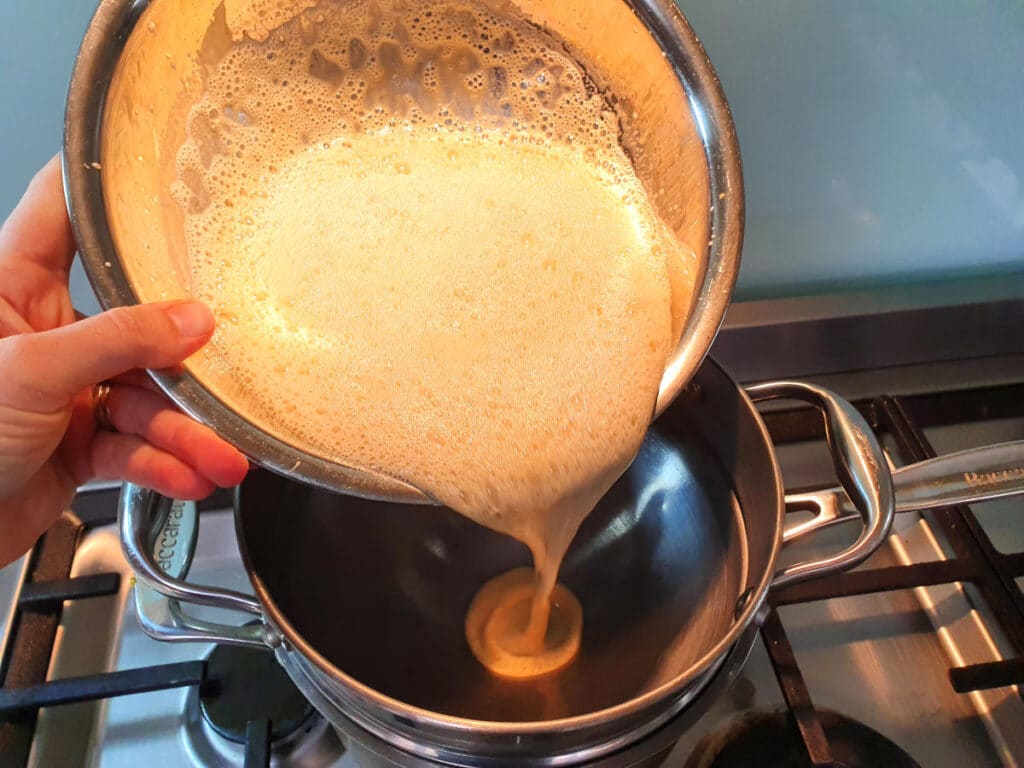 adding egg yoke, sugar and milk mix to double boiler on stove.