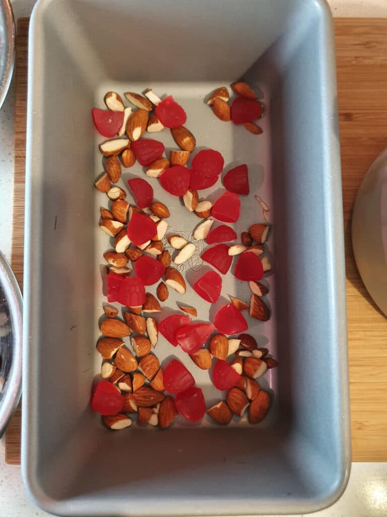 adding first layer of chopped raspberry candy to bottom of chilled ice cream storage container.