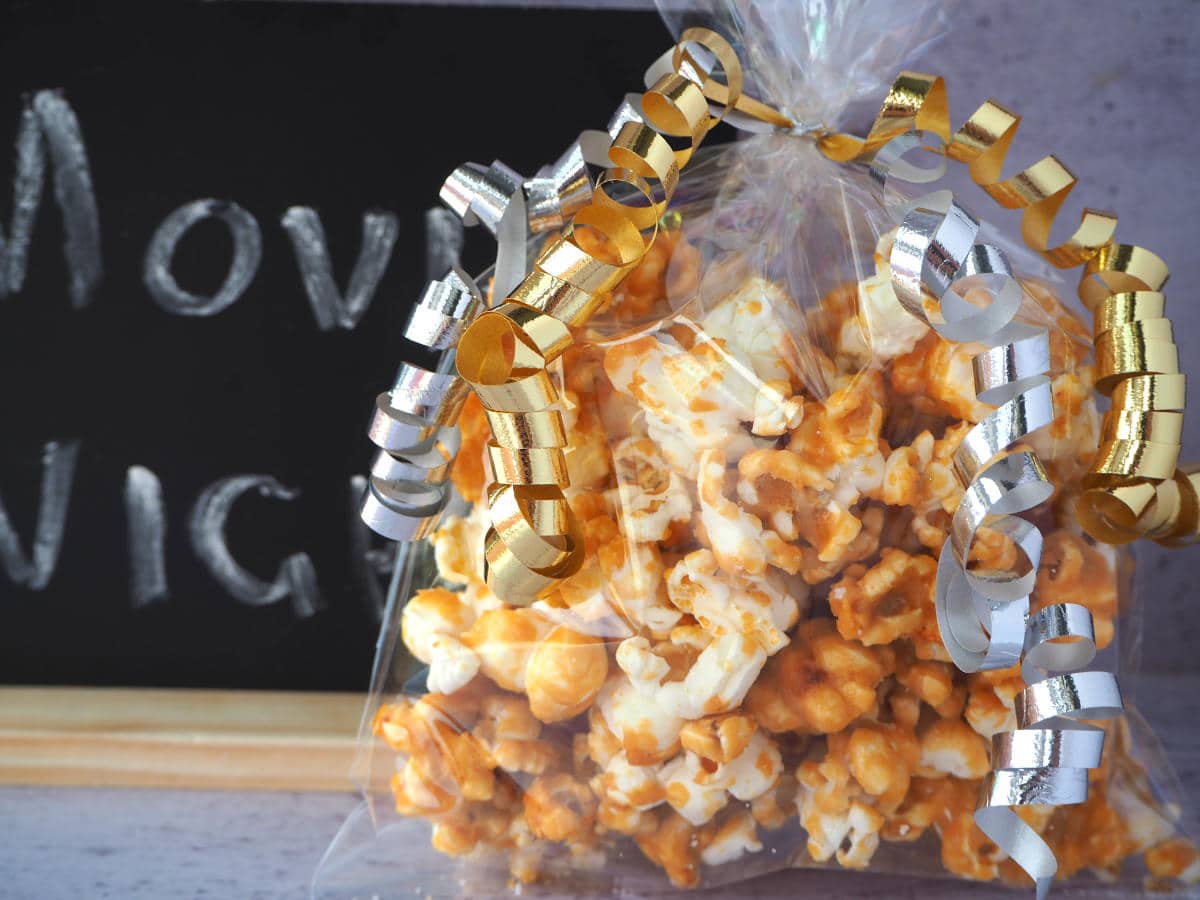Close up of bag of caramel popcorn in a clear cellophane gift bag, with silver and gold curling ribbon around the top, and a chalk board with Movie Night written on it.