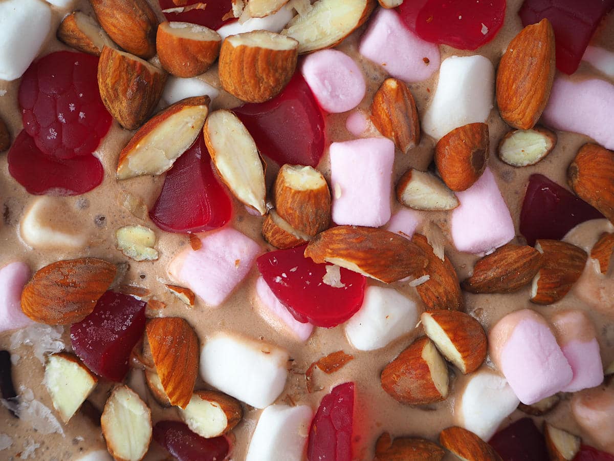 Top down close up view of rocky road ice cream with mini marshmallows, chopped almonds and raspberry candies.