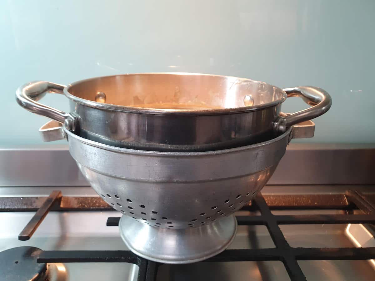 double boiler resting in colander to cool.