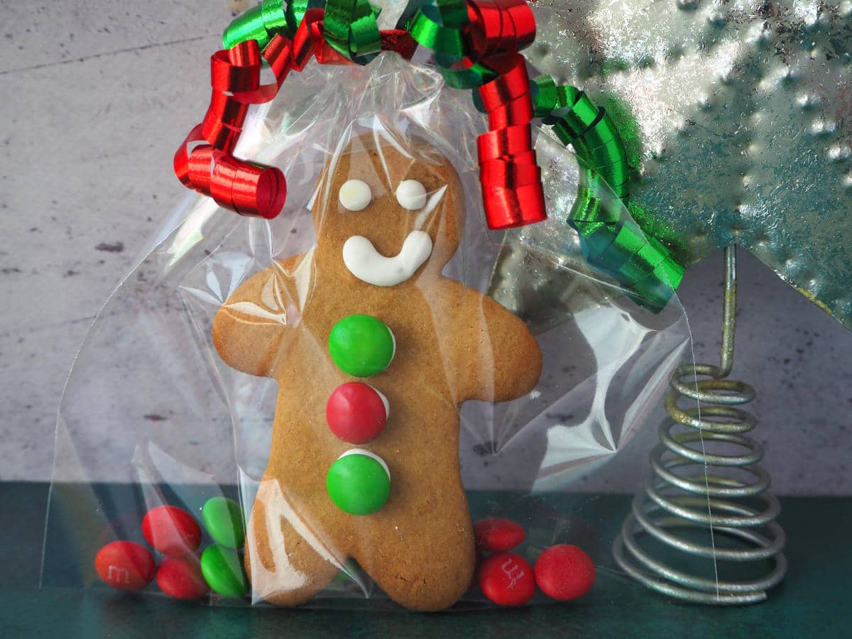 gingerbread man made up as a gift in a clear cellophane bag with red and green M&Ms and green and red curling ribbon around the top, with a silver tree top start to the right.