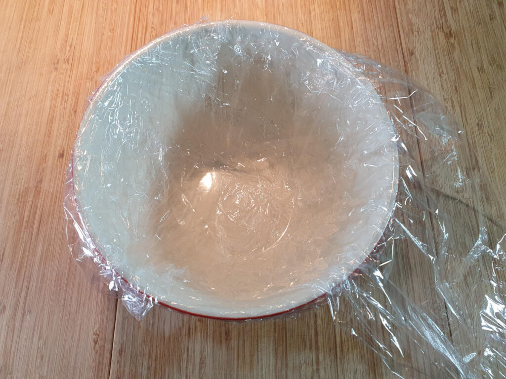 Lining pudding bowl with second layer of cling film, cross ways from last one so all of bowl is covered, with large overhang to cover top of pudding at the end.
