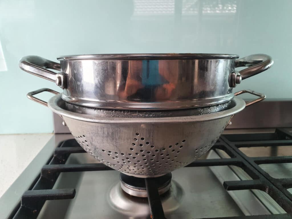 top of double boiler sitting in colander for stability when cooling.