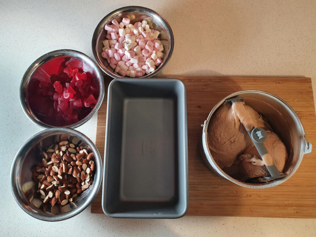 setting up mix ins with bowl of chopped almonds, chopped raspberries, mini marshmallows, chilled ice cream storage container and churned milk chocolate ice cream.