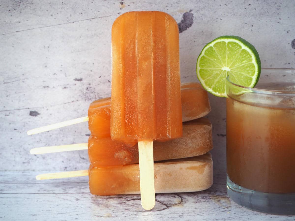 Cola popsicles 23 Stack of three cola popsicles, with one popsicle leaned again them forward facing, next to a glass of homemade cola with a round lime garnish.