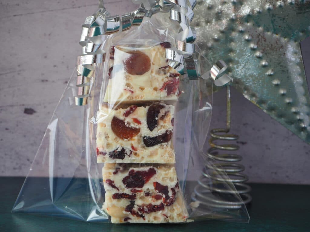 Stack of three cubes of white Christmas in a clear cellophane bag with silver curling ribbon tied around the top as a Christmas gift, with a metal silver start in the background.