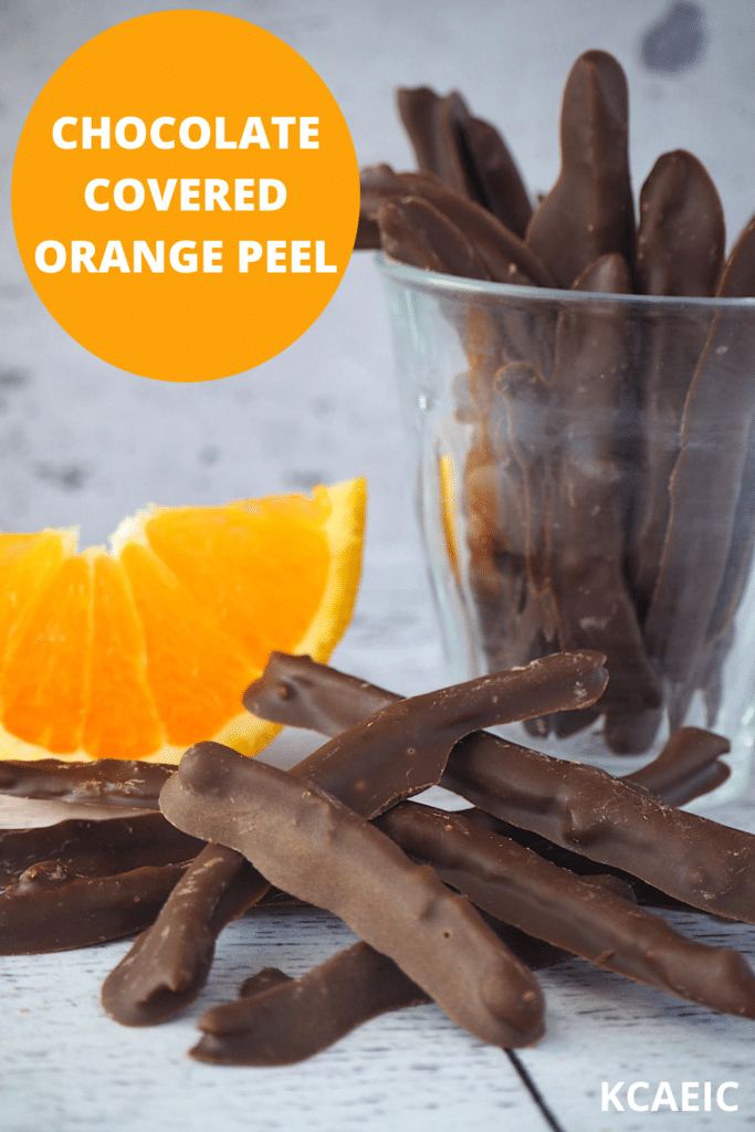 Chocolate covered orange peel with glass of chocolate covered orange peel, fresh sliced orange in background and text overlay, chocolate covered orange peel and KCAEIC.