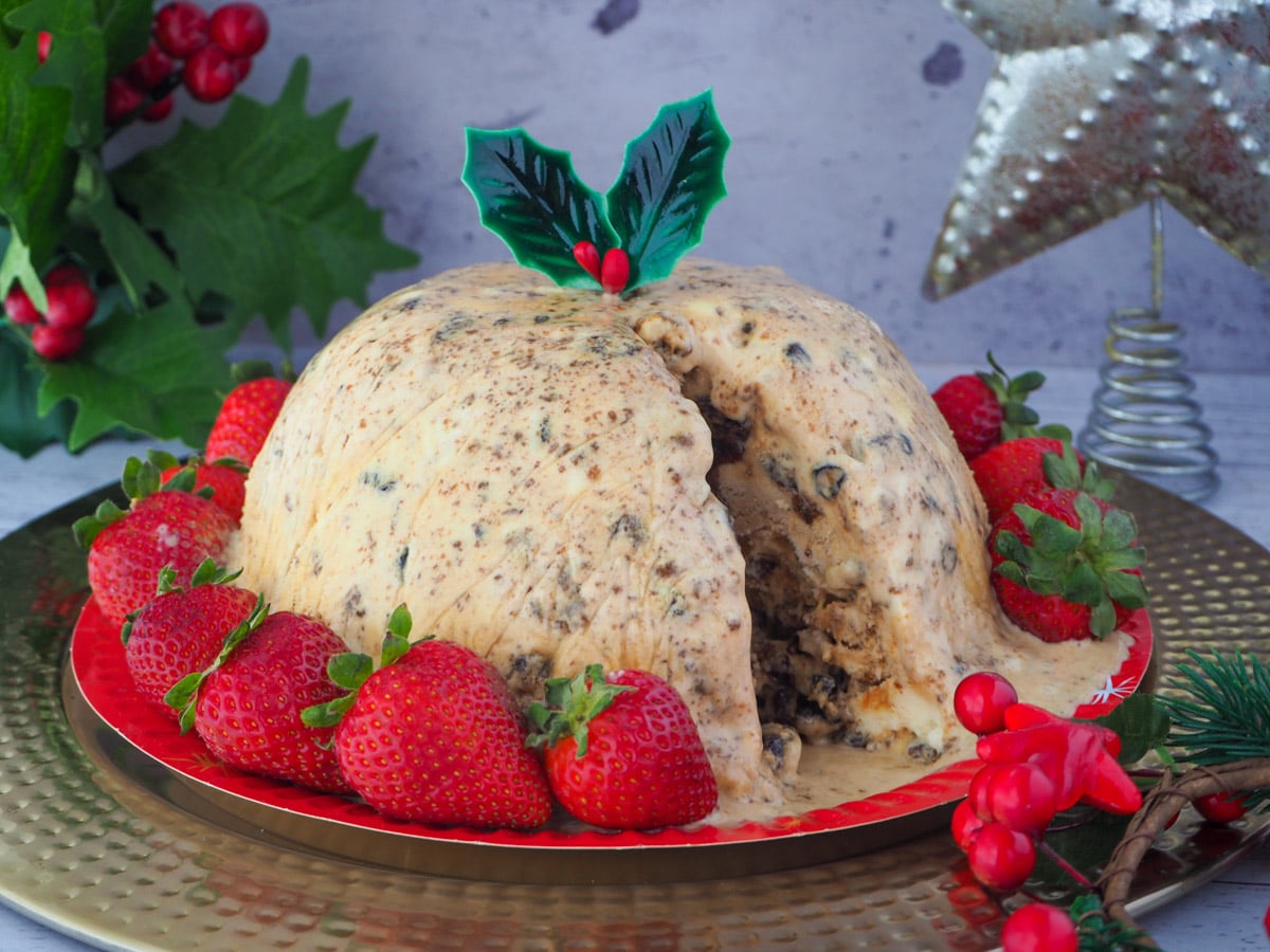 Christmas pudding ice cream a serve cut out, with holly garnish, surrounded by fresh strawberries, with holly and a Christmas star in the background