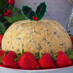 Christmas pudding ice cream with holly garnish, surrounded by fresh strawberries, with holly and a Christmas star in the background