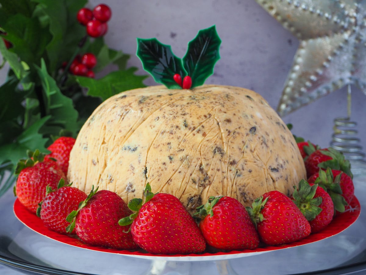 Christmas pudding ice cream with holly garnish, surrounded by fresh strawberries, with holly and a Christmas star in the background