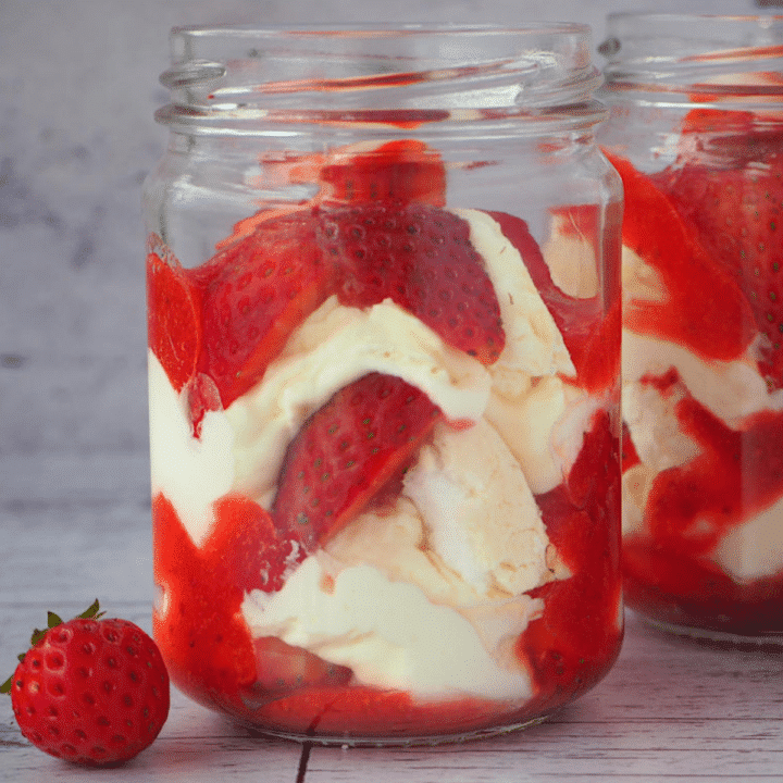 Two jars of Eton mess with fresh strawberries on the side.