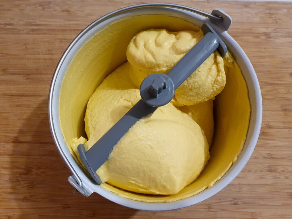 top down view churned mango ice cream in churning bowl.