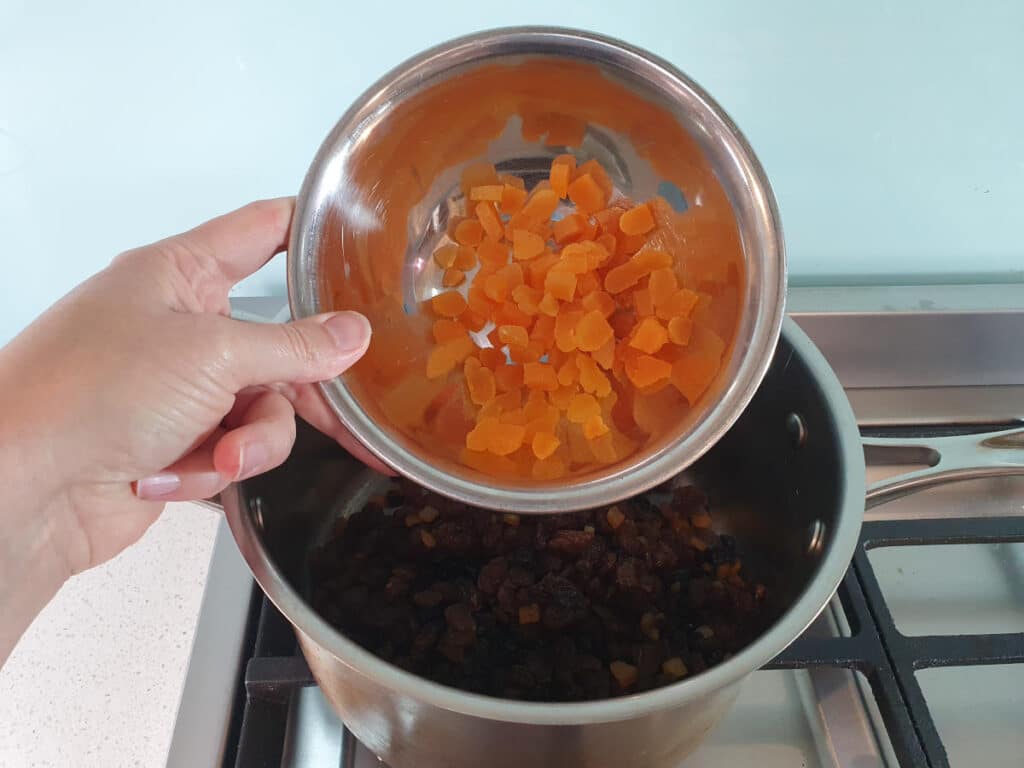 adding chopped dried apricots to pot on stove.