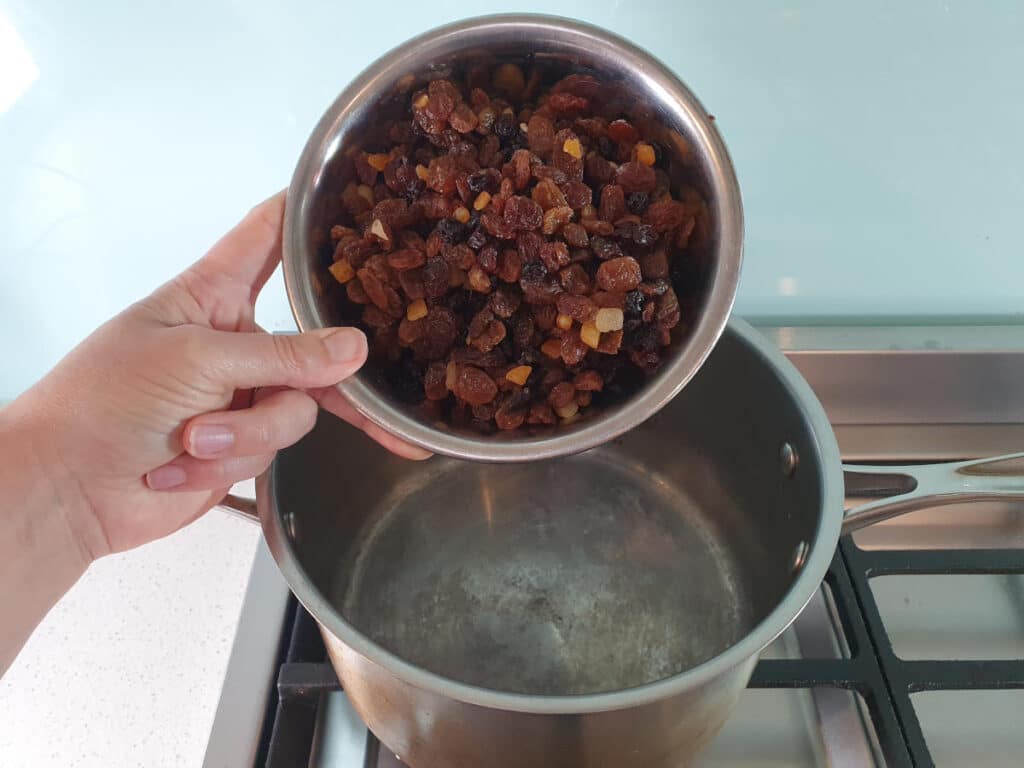 adding mixed dried fruit to pot on stove.