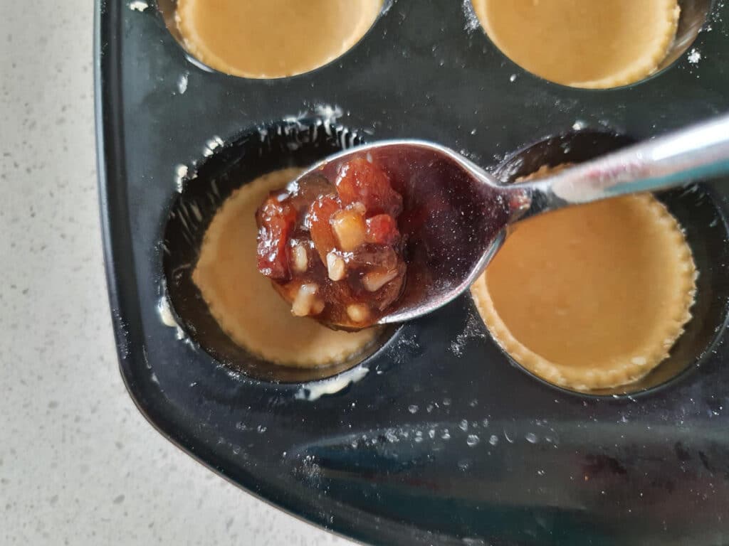 spooning fruit mince into tart cases.