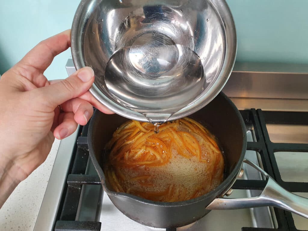 adding more water to candying peel in pot on stove.