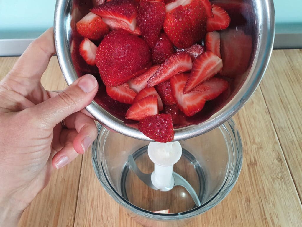 adding strawberries to food processor for sauce.