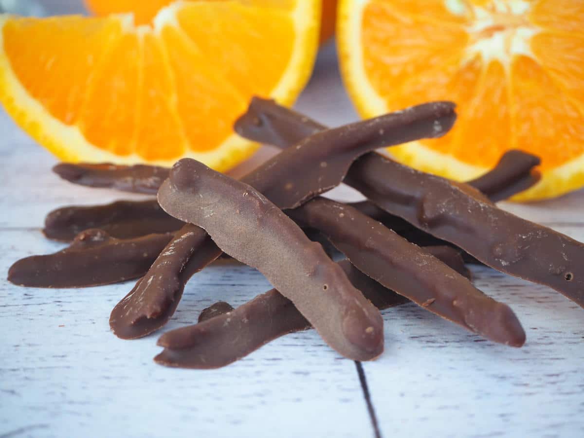 Chocolate covered orange peel with fresh slices of orange in background.