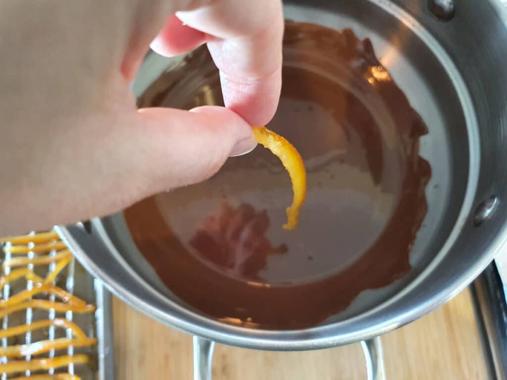 dropping one piece of candied orange peel into melted chocolate.