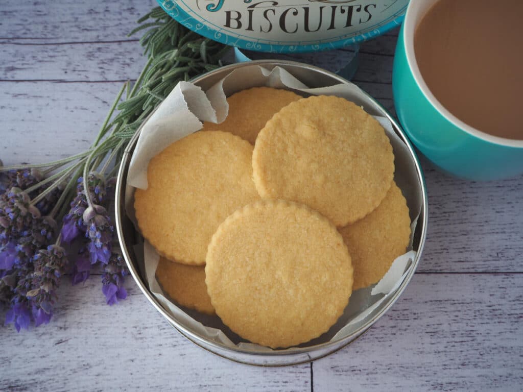 Gluten free shortbread 16 top down view gluten free shortbread in a biscuit tin, with a cup of tea and fresh lavender on the side.
