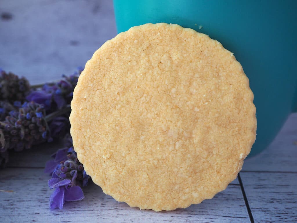 Side view of gluten free shortbread propped up against a teal mug, with fresh lavender on the side.