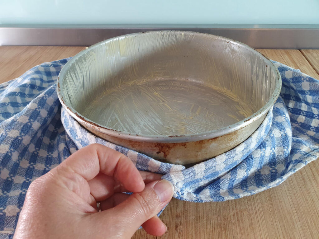 measuring circumference of cake tin with a teatowl.