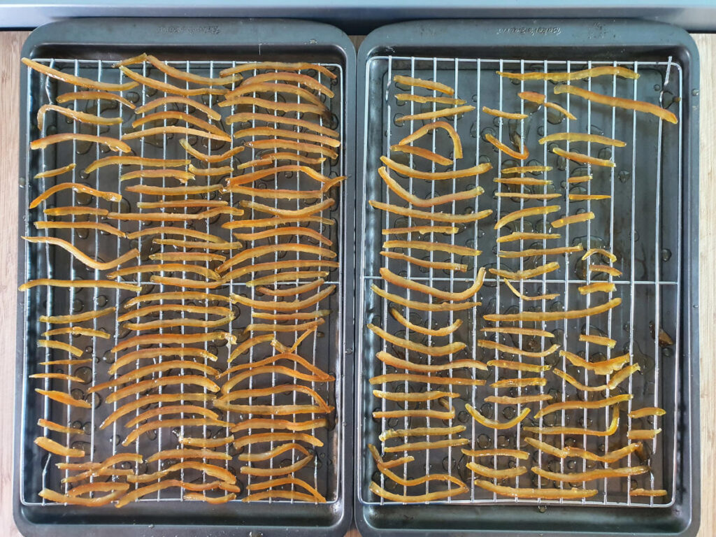 two tray of candied peel laid out on cooling racks on top of baking tray to catch the drips.