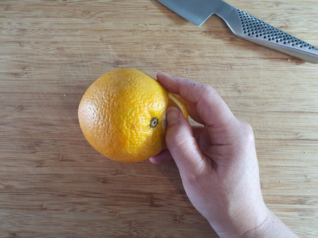 carefully peeling skin away from orange that has been scored into quarters.