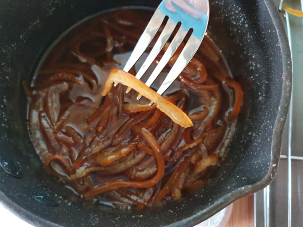 picking up candied peel from pot with a fork and shaking off excess syrup.