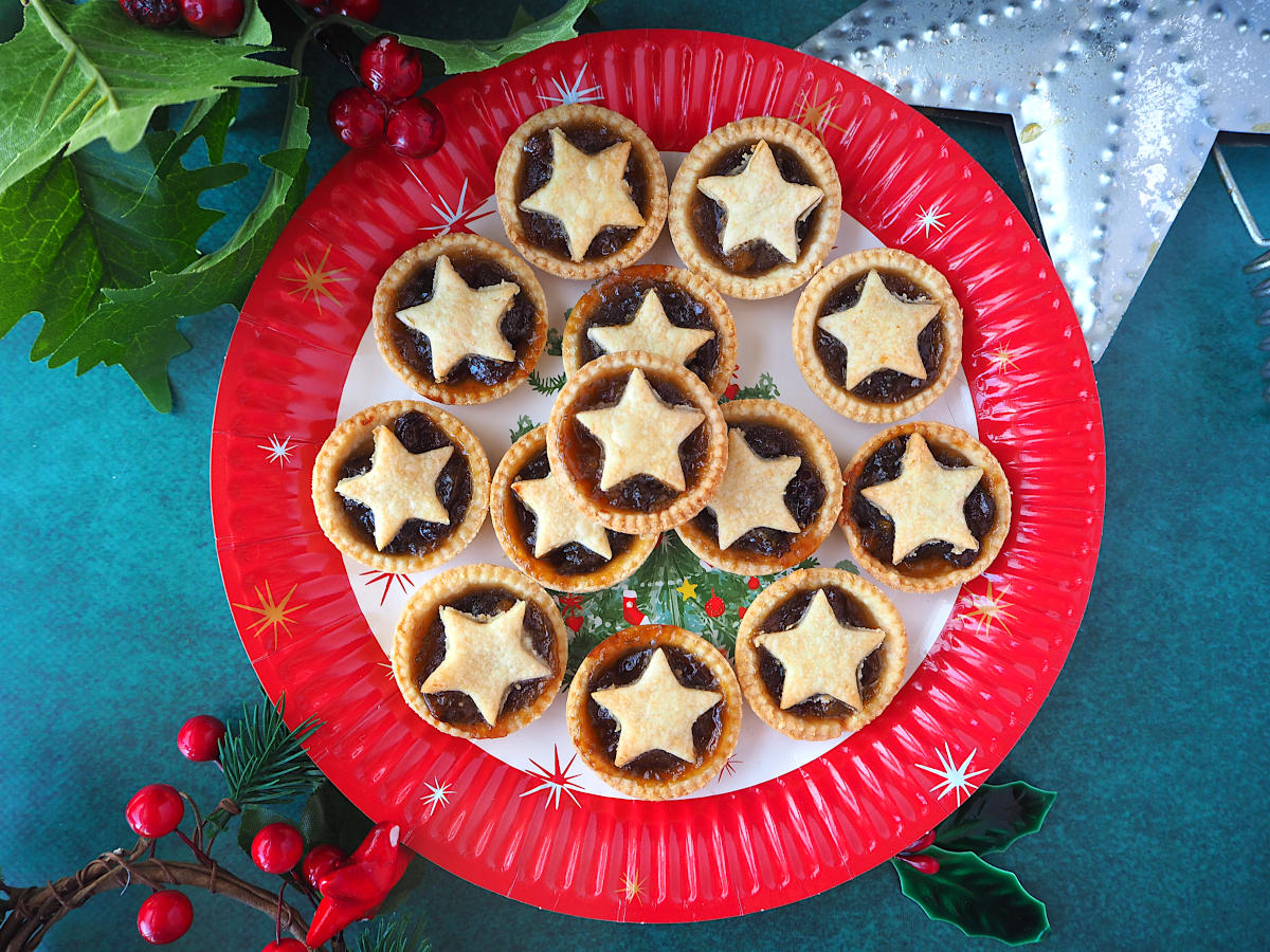 Top down view of mincemeat tarts on a Christmas plate, with Christmas decorations around it.